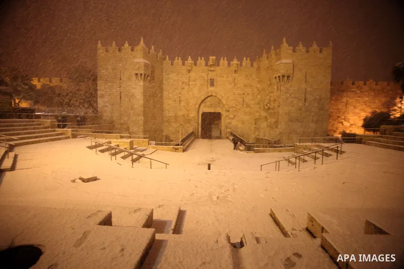 People walk in front of Damascus gate during a snowstorm in Jerusalem's Old City on December 12, 2013. Jerusalem is covered with snow Thursday, the heaviest snow storm hitting the city since 1953 as meteorologists dubbed...