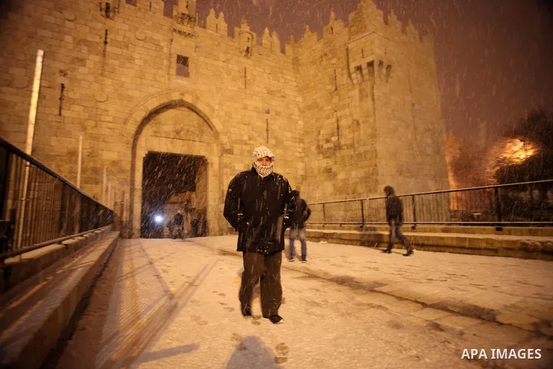 People walk in front of Damascus gate during a snowstorm in Jerusalem's Old City on December 12, 2013. Jerusalem is covered with snow Thursday, the heaviest snow storm hitting the city since 1953 as meteorologists dubbed...