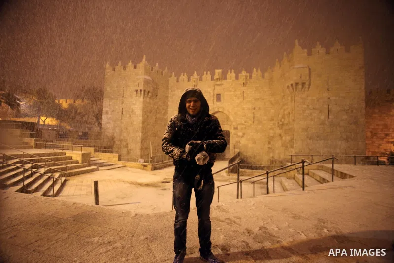 A Palestinian man poses for a photograph in front of Damascus gate during a snowstorm in Jerusalem's Old City on December 12, 2013. Jerusalem is covered with snow Thursday, the heaviest snow storm hitting the city since...