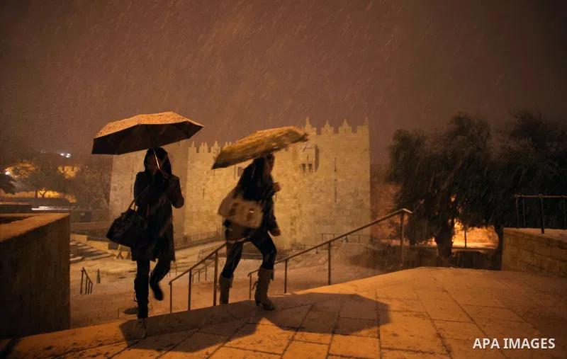 People walk in front of Damascus gate during a snowstorm in Jerusalem's Old City on December 12, 2013. Jerusalem is covered with snow Thursday, the heaviest snow storm hitting the city since 1953 as meteorologists dubbed...
