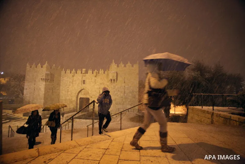 People walk in front of Damascus gate during a snowstorm in Jerusalem's Old City on December 12, 2013. Jerusalem is covered with snow Thursday, the heaviest snow storm hitting the city since 1953 as meteorologists dubbed...