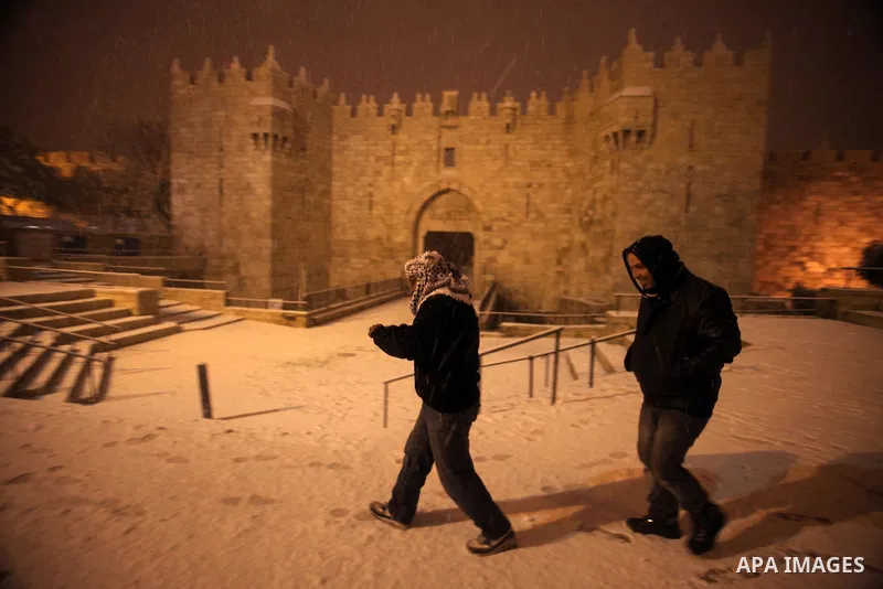 People walk in front of Damascus gate during a snowstorm in Jerusalem's Old City on December 12, 2013. Jerusalem is covered with snow Thursday, the heaviest snow storm hitting the city since 1953 as meteorologists dubbed...