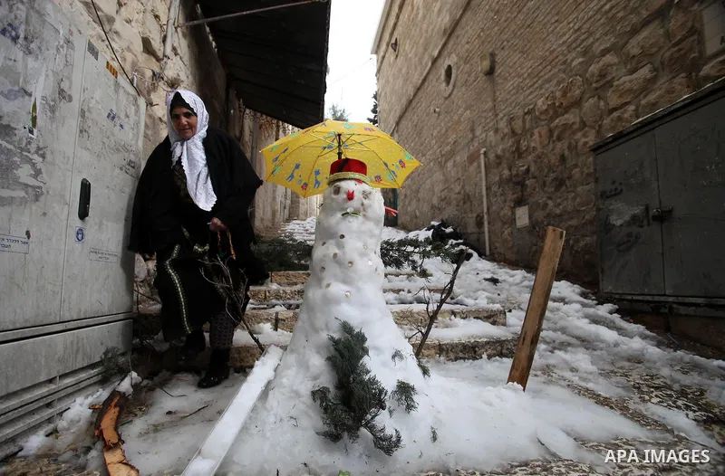 A Palestinian woman walks past a snowman in Jerusalem's Old City following a snowstorm on December 13, 2013. The hilltop city of Jerusalem was paralysed today by its fiercest snowstorm in years, with its mayor calling ou...