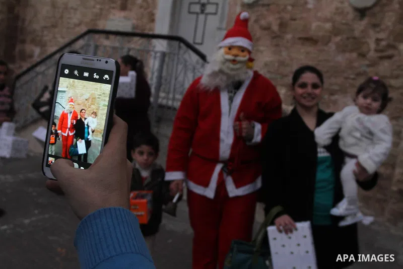 A Palestinian man dressed up as Santa Claus with Christians pose for a photograph during a ceremony ahead of Christmas at the Church of Saint Porphyrius, in Gaza City on 22 December 2013. Photo by Mohammed Asad