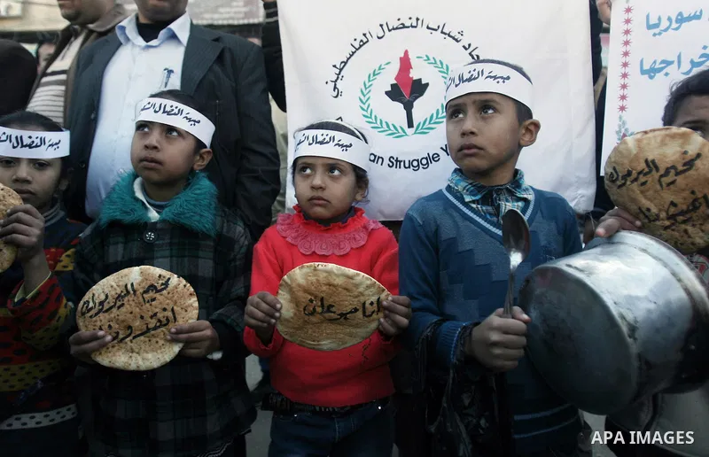 Palestinian children take part in a rally to show solidarity with Palestinian refugees in Syria's main refugee camp Yarmouk, in Rafah in the southern Gaza Strip January 8, 2014. The Arabic words on the bread read, " I am...