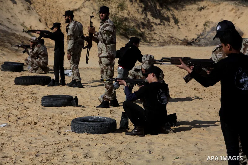A member of Palestinian security forces teaches a Palestinian high school student how to use a weapon during a military-styled exercise routine at a course conducted by the Hamas-run ministry of education, in Rafah in th...