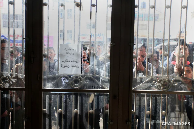 Palestinian protesters look through broken glass doors of a gate at a hotel where a group of Israeli and Palestinian peace activists hold a meeting in the West Bank city of Ramallah, Thursday, Jan. 9, 2014. Protesters sa...