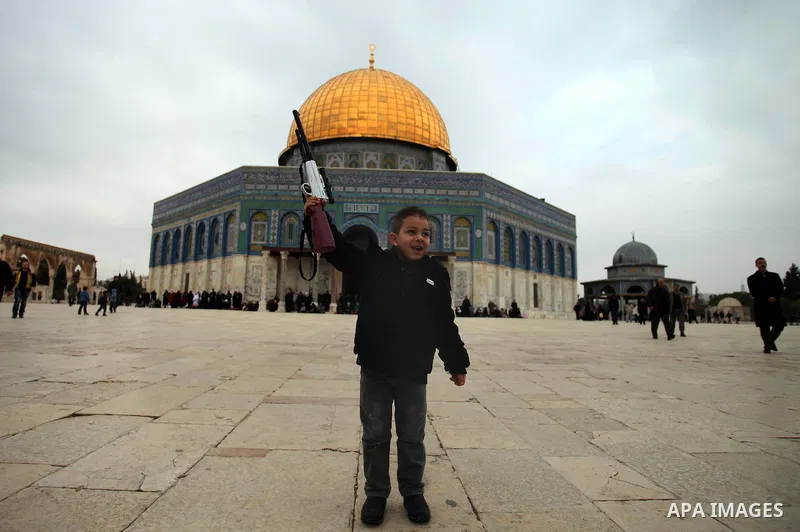 A Palestinian boy plays with his gun toy in front of the Dome of the Rock mosque following Friday prayers at the Al-Aqsa compound, Islam's third holiest site, in the old city of Jerusalem January 10, 2014. Photo by Saeed...