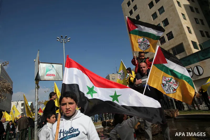Palestinian supporters of Fatah movement hold national and movement flags during a demonstration in solidarity with Palestinian refugees in Yarmouk refugee camp in the suburbs of the Syrian capital of Damascus, in the We...