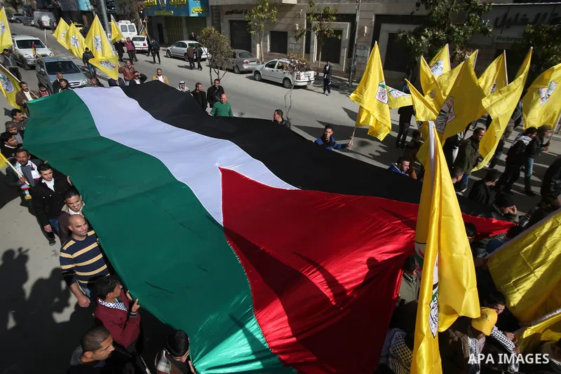 Palestinian supporters of Fatah movement hold national and movement flags during a demonstration in solidarity with Palestinian refugees in Yarmouk refugee camp in the suburbs of the Syrian capital of Damascus, in the We...