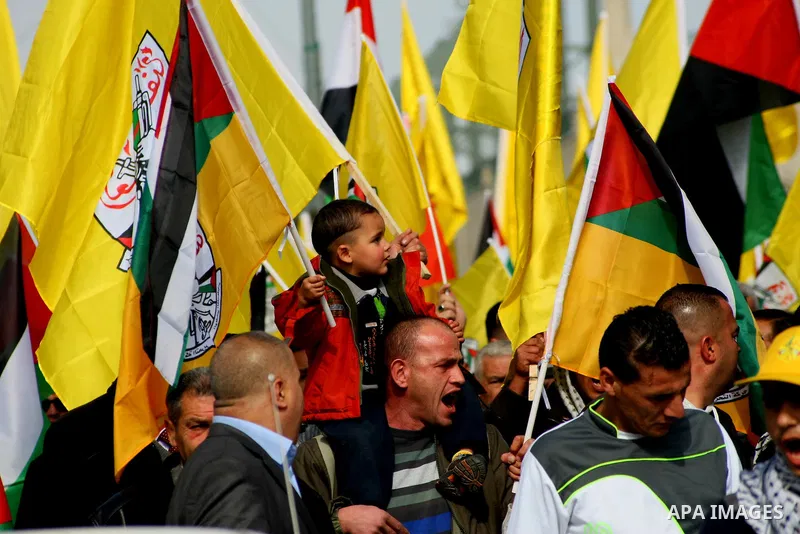 Palestinian supporters of Fatah movement hold national and movement flags during a demonstration in solidarity with Palestinian refugees in Yarmouk refugee camp in the suburbs of the Syrian capital of Damascus, in the We...
