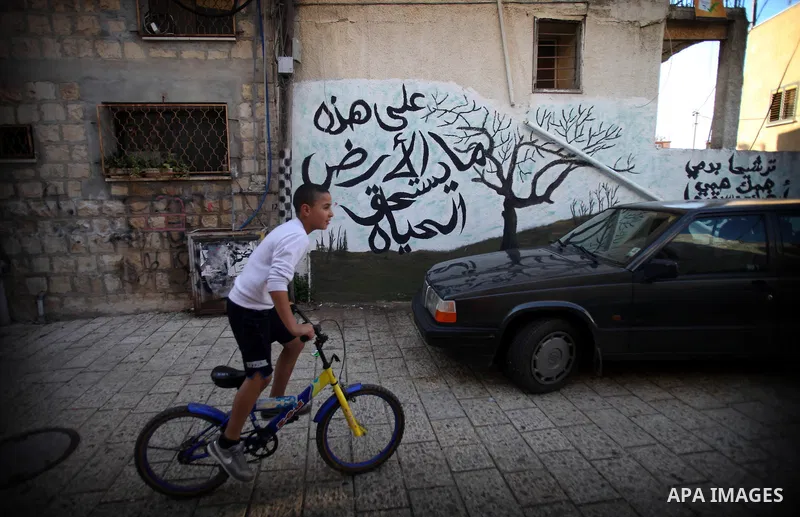 A Palestinian boy rides his bicycle past a graffiti reads in Arabic "On this earth what makes life worth living" on a wall in the village of Tarshiha, north Acre on January 21, 2014. Tarshiha was in the territory allotte...