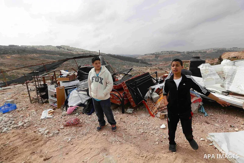 Palestinian boys stand next to their furniture as bulldozers demolish their house in the the Beit Hanina neighborhood of East Jerusalem, January 27, 2014. Israeli authorities on Monday demolished four Palestinian homes i...
