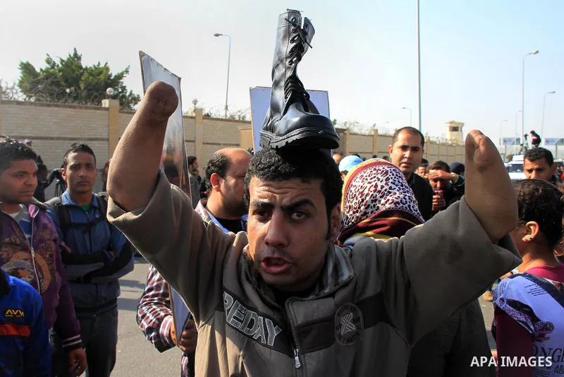 A supporter of Egypt's army chief Field Marshal Abdel Fattah al-Sisi holds a military boot on his head as a sign of support for military rule, during a demonstration outside a police academy on the outskirts of Cairo Jan...
