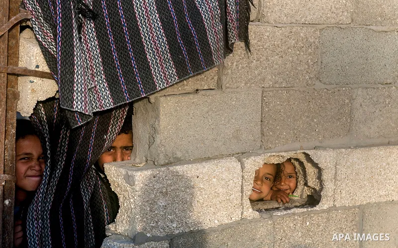 Palestinian children look through holes in a wall at their family's house at al-Shati refugee camp in the west Gaza City on January 30, 2014. Photo by Abdullah Jadallah