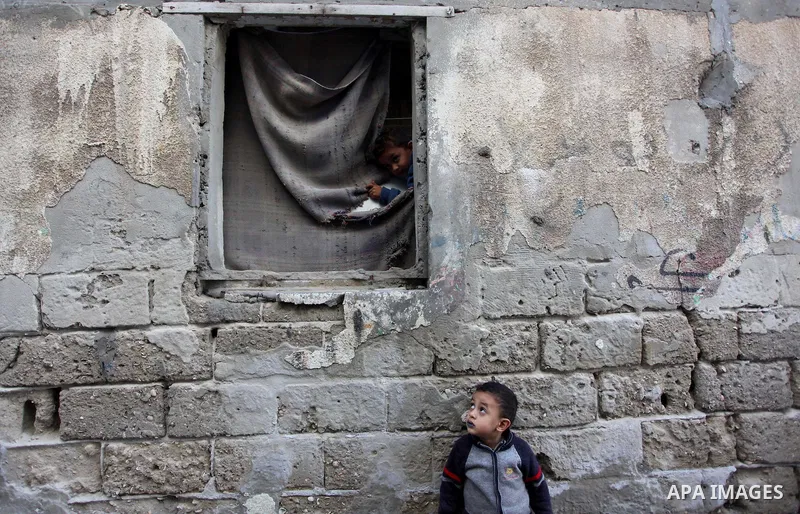 A Palestinian boy looks through a window as another looks on outside his family's house at al-Shati refugee camp, in the west Gaza City on February 02, 2014. Photo by Ashraf Amra