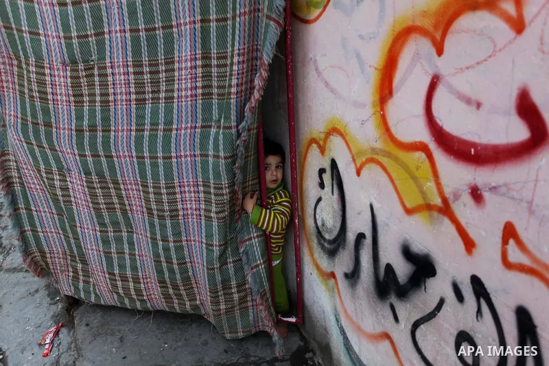 A Palestinian child looks on behind a curtain at the entrance of family's house at al-Shati refugee camp, in the west Gaza City on February 02, 2014. Photo by Ashraf Amra