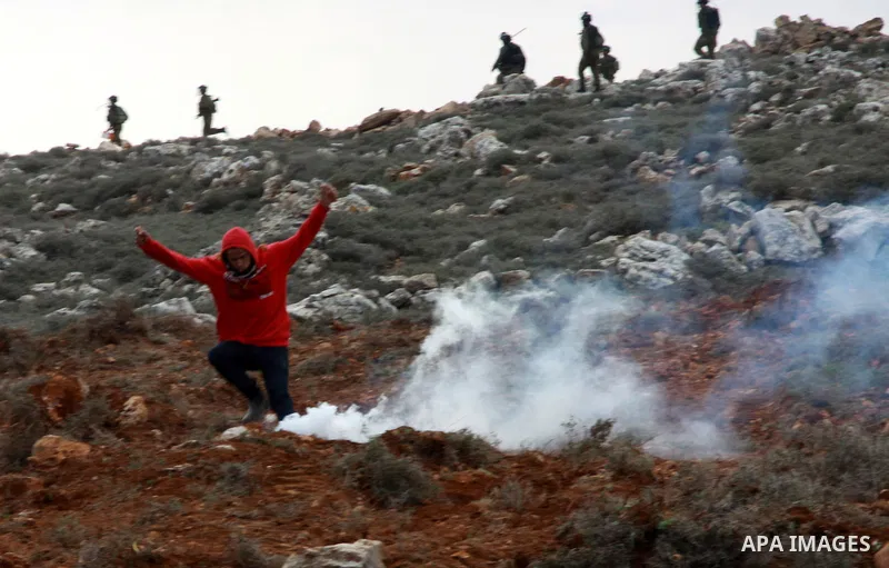 A Palestinian youth runs seek for cover from tear gas fired by Israeli security forces during clashes following a confrontation between Palestinians and Jewish settlers, in the West Bank village of Qusra, near Nablus, Fe...