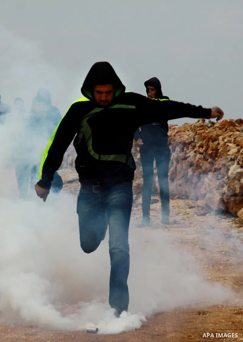 A Palestinian youth kicks back a tear gas canister fired by Israeli security forces during clashes following a confrontation between Palestinians and Jewish settlers, in the West Bank village of Qusra, near Nablus, Feb....