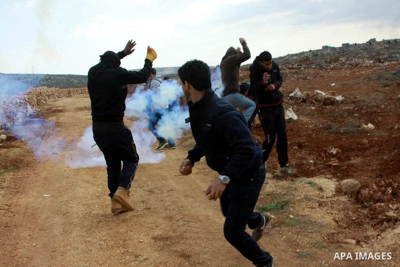 Palestinian youth run seek for cover from tear gas fired by Israeli security forces during clashes following a confrontation between Palestinians and Jewish settlers, in the West Bank village of Qusra, near Nablus, Feb....