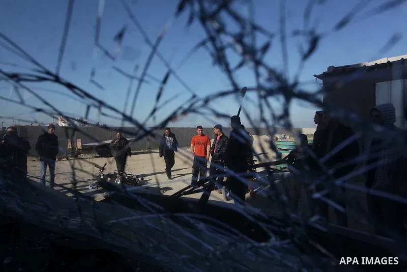 Palestinians are seen through a damaged car window as they look at the scene of an Israeli air strike in the centre of the Gaza Strip February 9, 2014. An Israeli air strike on the Gaza Strip on Sunday critically wounded...