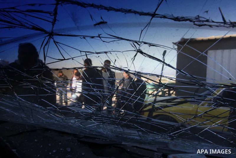 Palestinians are seen through a damaged car window as they look at the scene of an Israeli air strike in the centre of the Gaza Strip February 9, 2014. An Israeli air strike on the Gaza Strip on Sunday critically wounded...