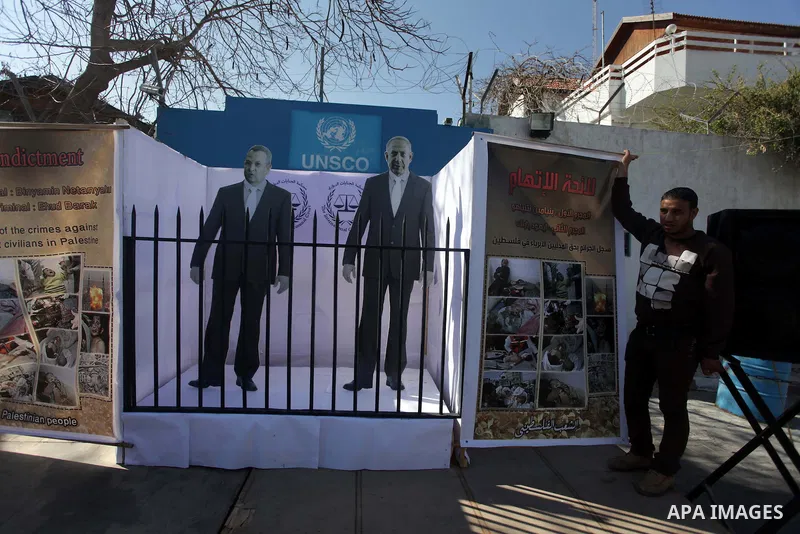 A Palestinian man stands near of images of the war criminals Prime Minister of Israel Benjamin Netanyahu, and former Prime Minister Ehud Barak during a moot court for them, in front of the headquarters of the United Stat...