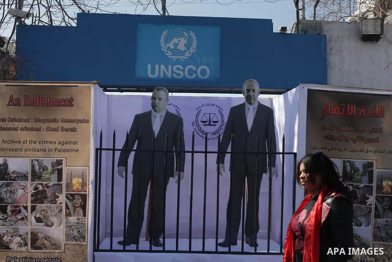 A Palestinian woman stands near of images of the war criminals Prime Minister of Israel Benjamin Netanyahu, and former Prime Minister Ehud Barak during a moot court for them, in front of the headquarters of the United Na...