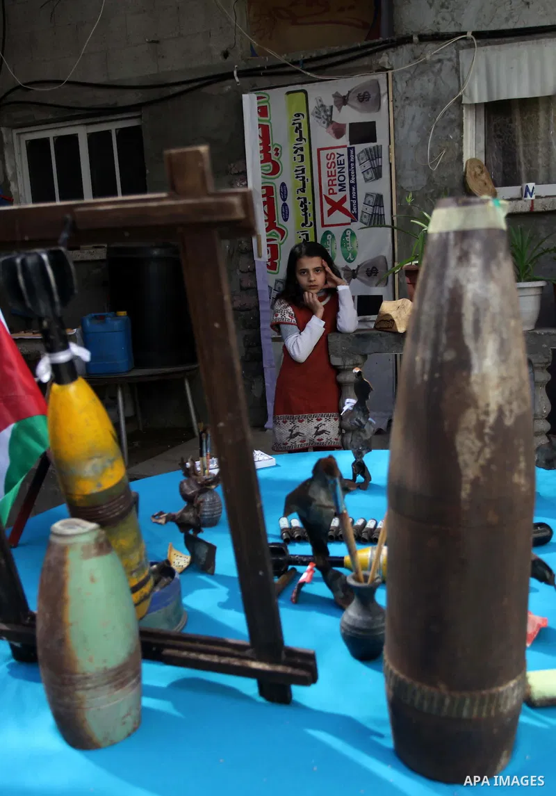 A girl watches as Palestinian Mohammed al-Zomar (not pictured), 32 works on the remains of Israeli ammunition at his studio in the central Gaza Strip February 12, 2014. Al-Zomar draws and paints on remains of Israeli amm...