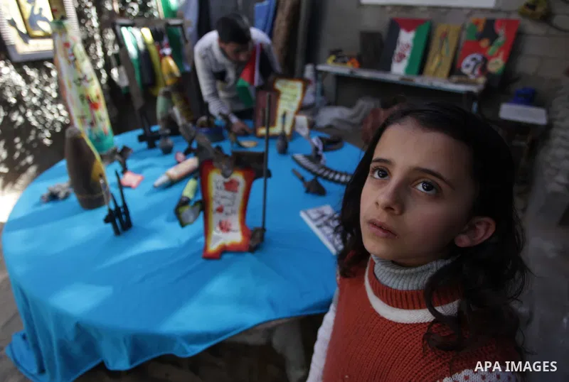 A girl watches as Palestinian Mohammed al-Zomar, 32 works on the remains of Israeli ammunition at his studio in the central Gaza Strip February 12, 2014. Al-Zomar draws and paints on remains of Israeli ammunition that he...