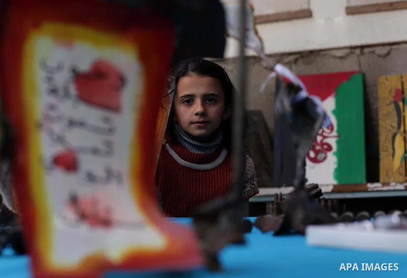 A girl watches as Palestinian Mohammed al-Zomar (not pictured), 32 works on the remains of Israeli ammunition at his studio in the central Gaza Strip February 12, 2014. Al-Zomar draws and paints on remains of Israeli amm...