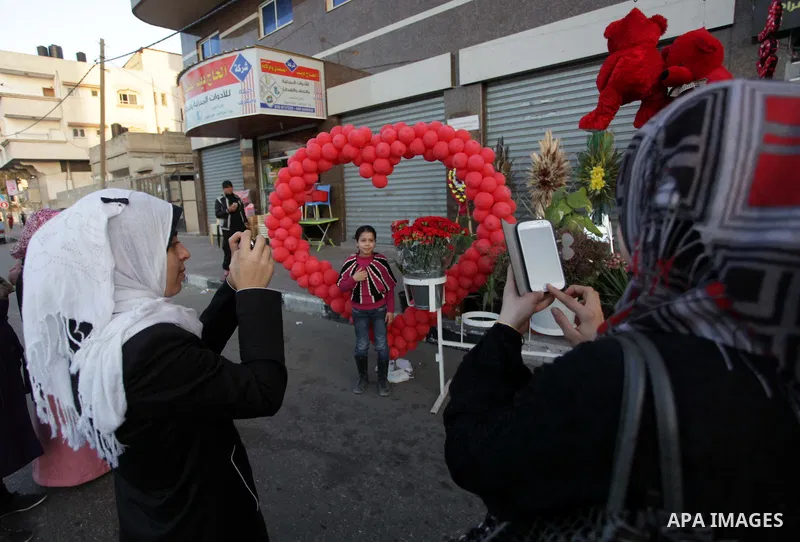 Palestinian girls take photo for a girl in front of a heart shaped from ballons ahead of Valentine's day in Gaza City on February 13, 2014. Valentine's Day is increasingly popular among younger Palestinians, many of whom...