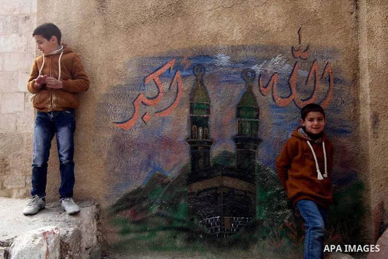 Palestinian boys stand in front a mural depicts the holy Kaaba, in Jerusalem's old City on February 14, 2014. Photo by Saeed Qaq