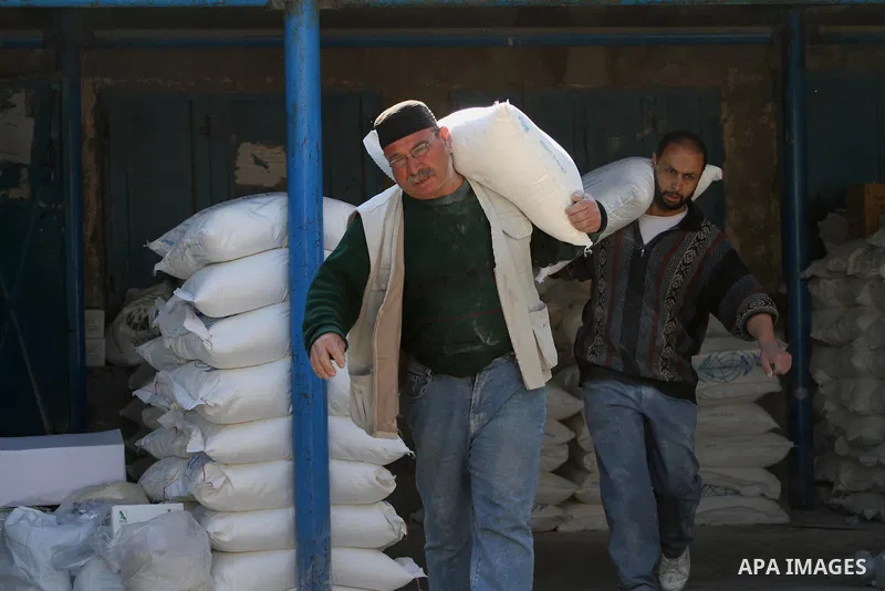 Palestinian men hold a sack of flour at monthly food aid at a UN distribution center in Gaza city, on Feb. 18, 2014. The UN Relief and Works Agency (UNRWA) will reduce some of its services for Palestinian refugees due to...