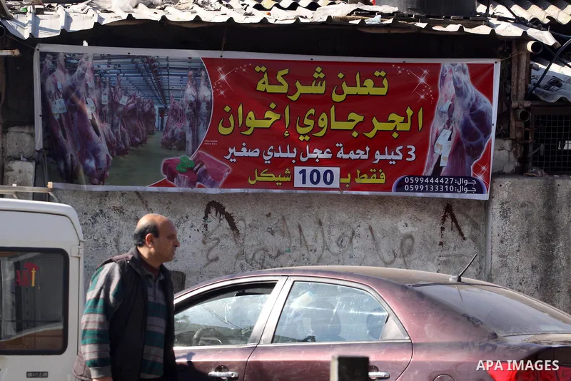 A Palestinian man walks past a billboard for a discount campaign on fresh meat prices in Gaza City on Feb. 19, 2014. Palestinian butchers campaign discounts on prices of fresh meat to confront the sharp reduction in dema...