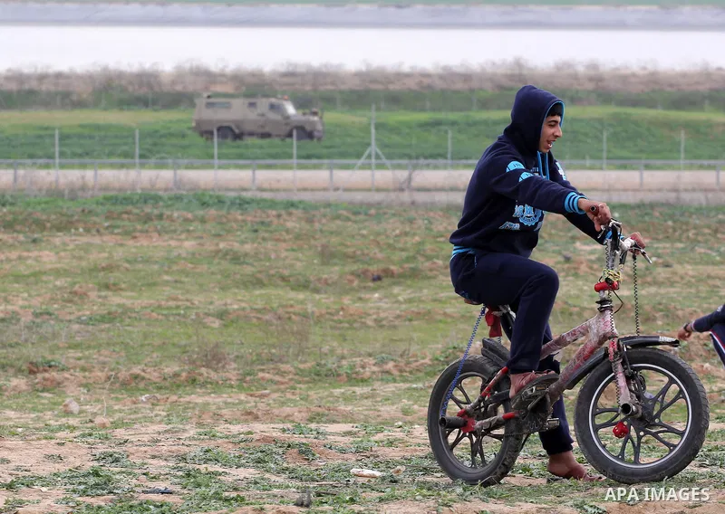 A young Palestinian rides a bicycle in front an Israeli military vehicle during clashes near the border with Israel, east of Jabalia refugee camp in northern Gaza Strip on February 21, 2014. The Israeli army fired live r...