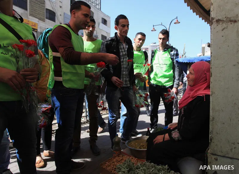 Palestinian youth distribute roses during a participate in the campaign " for the good, we gather" honoring for the elderly working women at the streets, in the West Bank city of Ramallah, on Feb. 22, 2014. Photo by Issa...