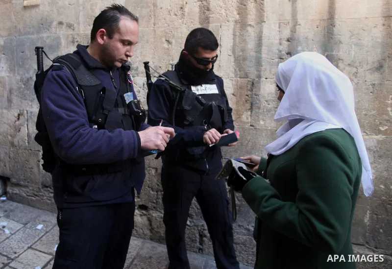 A member of the Israeli security forces checks the ID of a Palestinian woman while he wait to cross an alleyway leading to the al-Aqsa Mosque compound on February 25, 2014 in the Old City of Jerusalem. Israeli police ear...