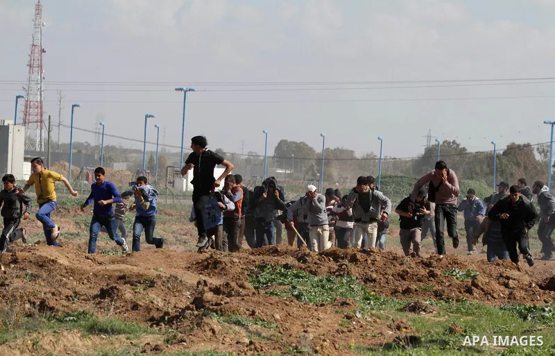 Palestinian protesters run seek for cover from tear gas fired by Israeli security forces during clashes near Nahal Oz border crossing with Israel, east of Gaza City, on February 25, 2014 following a demonstration to comm...