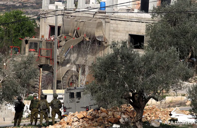 Israeli soldiers stand guard as an army bulldozer demolishes the house of Palestinian Moataz Washaha, who died during an Israeli army raid on his home in the northern West Bank town of Bir Zeit, near Ramallah on February...
