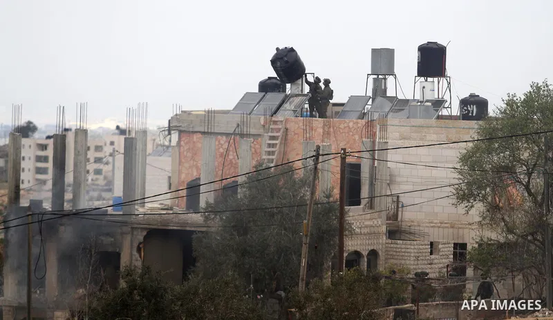 Israeli soldiers remove a water tank from the house of Palestinian Moataz Washaha, who died during an Israeli army raid on his home in the northern West Bank town of Bir Zeit, near Ramallah on February 27, 2014. Israeli...