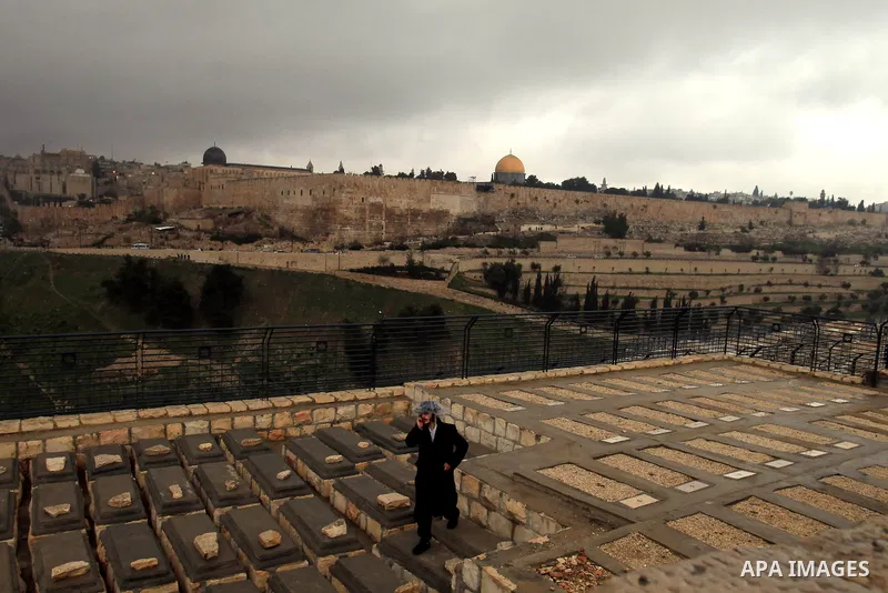 An Ultra-Orthodox Jewish man walks at the Jews cemetery in Ras al-Amud during a hazy and cloudy weather, in Jerusalem's Old City March 09, 2014, The Dome of the Rock mosque is seen in the background. Photo by Saeed Qaq