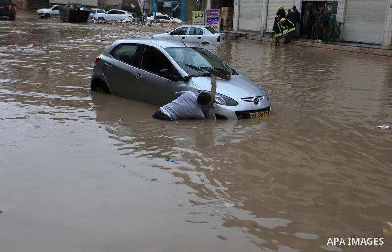 A Palestinian man tries to remove a car submerged in a flooded street during heavy rains on a stormy day, in the West Bank village of Kufr Aqab, northern Jerusalem on March 12, 2014. Photo by Issam Rimawi