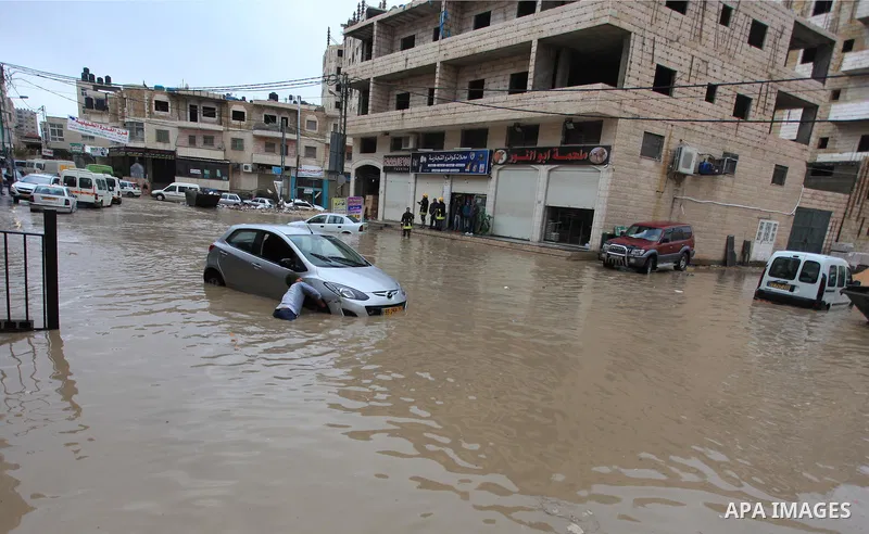 A Palestinian man tries to remove a car submerged in a flooded street during heavy rains on a stormy day, in the West Bank village of Kufr Aqab, northern Jerusalem on March 12, 2014. Photo by Issam Rimawi