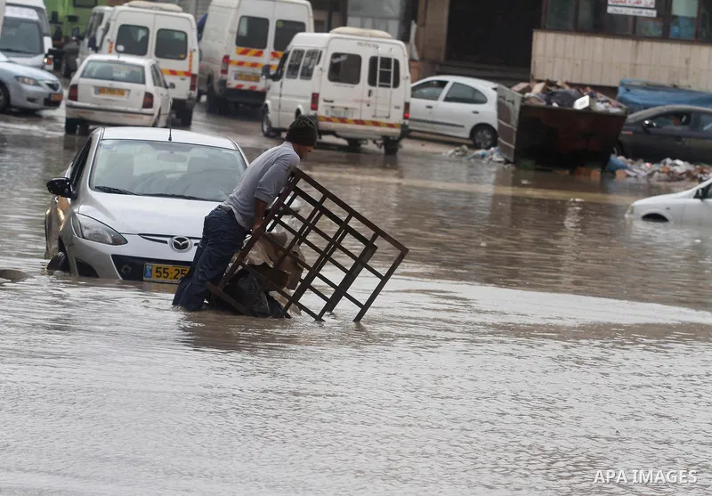 A Palestinian man tries to remove a car submerged in a flooded street during heavy rains on a stormy day, in the West Bank village of Kufr Aqab, northern Jerusalem on March 12, 2014. Photo by Issam Rimawi