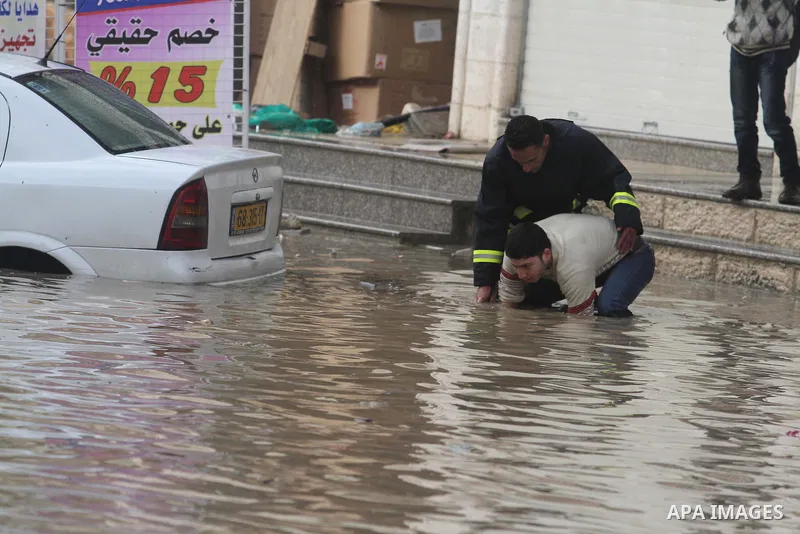 Palestinian civil defence try to remove a car submerged in a flooded street during heavy rains on a stormy day, in the West Bank village of Kufr Aqab, northern Jerusalem on March 12, 2014. Photo by Issam Rimawi