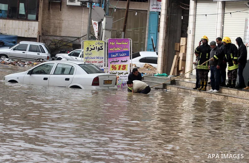 Palestinian civil defence try to remove a car submerged in a flooded street during heavy rains on a stormy day, in the West Bank village of Kufr Aqab, northern Jerusalem on March 12, 2014. Photo by Issam Rimawi