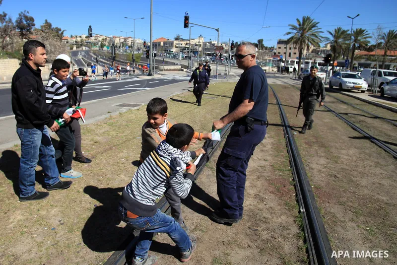 An Israeli police officer tries to take down a Palestinian flag from children during a protest against the annual Jerusalem Marathon in the Old City on March 21, 2014. More than 15,000 runners from 50 different countries...