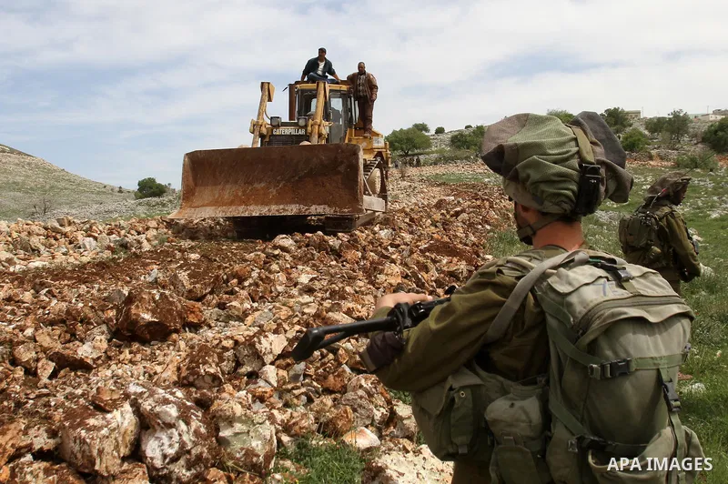 Israeli security forces stand guard in front of a Palestinian farmer as he rides his bulldozer, in the West Bank village of Burin south of Nablus, March 23, 2014. Clashes broke out Sunday morning after Jewish settlers fr...