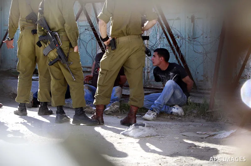 Israeli soldiers guard three Palestinians who were handcuffed with plastic cords after being arrested following clashes between Palestinians and Israeli soldiers in the West Bank city of Hebron, 28 March 2014. Photo by M...
